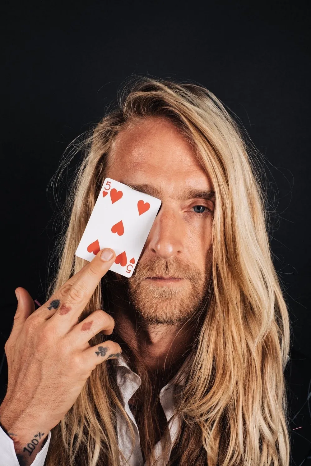 James Fabulous holding a five of hearts playing card across one eye
